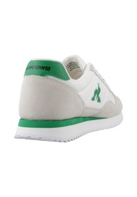 Sneaker bianco con accenti grigi in suede e branding verde sul tallone, dotato di suola testurizzata e dettaglio del logo sul lato.