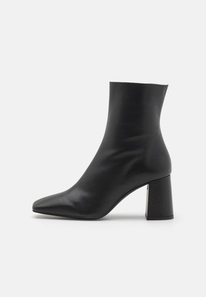 Botín negro de tobillo hecho de cuero liso, con puntera puntiaguda y tacón cuadrado grueso. Diseño elegante con un eje ajustado.