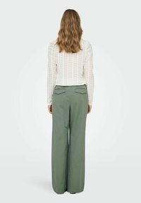 White patterned top with long sleeves, paired with high-waisted, wide-leg green pants, viewed from the back.