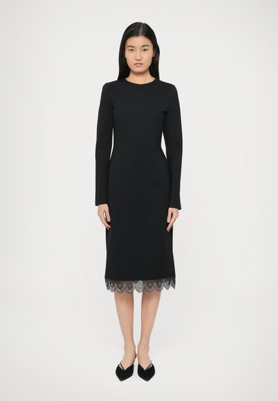 Robe noire à manches longues avec une silhouette ajustée ; dotée d'un ourlet en dentelle festonné. Texture douce, longueur au genou et encolure simple.