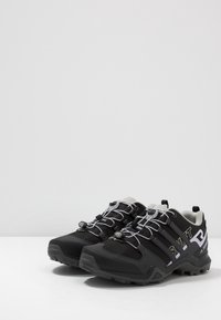 Musta ulkokenkä harmailla yksityiskohdilla, verkkokankaalla ja synteettisillä materiaaleilla, jossa on kuvioitu pohja, kontrastiväriset nauhat ja turvallinen kiinnitysjärjestelmä.