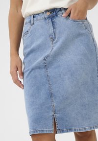 Lichtblauwe denimrok met een slim-fit ontwerp, vooruitsnijding en gestikte accenten. Voorzien van vier zakken en een knoopsluiting in de taille.