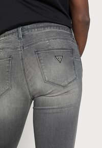 Vaqueros gris oscuro de mezclilla con corte ajustado. Presenta dos bolsillos traseros y un logo triangular negro en el bolsillo derecho.