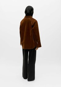 Braunes Cordhemd mit Kragen, langen Ärmeln und Knopfakzenten, kombiniert mit schwarzen Hosen mit weitem Bein. Einfaches und strukturiertes Design.