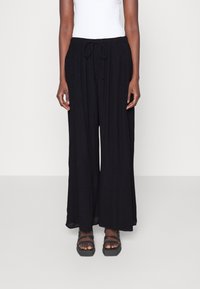 Pantalons larges noirs en tissu léger. Dotés d'une taille élastique avec un cordon de serrage. Texture lisse avec une silhouette fluide.