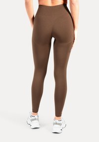 Bruine leggings met hoge taille gemaakt van rekbare stof, met een gladde textuur en een aansluitend ontwerp. Gecombineerd met witte sportschoenen.