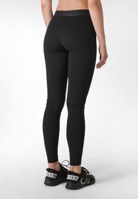 Mustat leggingit korkealla vyötäröllä ja tiukalla muotoilulla, joissa on sileä pinta ja hienovaraiset rypytykset nilkoissa, yhdistettynä mustiin kenkiin.