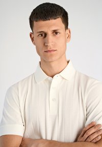 Biała, rybka polo z kołnierzykiem, z zapięciem na guziki i krótkimi rękawami. Gładka faktura, dopasowany krój, minimalne detale.