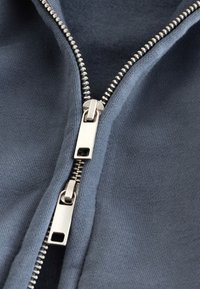 Hoodie met ritssluiting in donkerblauwe stof met geribbelde textuur. Voorzien van dubbele metalen ritsen en een gladde voering bij de opening.