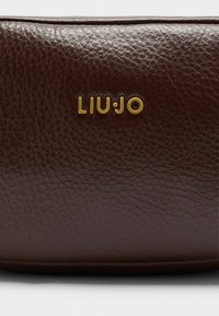 Smeđa kožna torbica s teksturiranim završetkom i zlatnim logom "LIU•JO" istaknuto prikazanim. Kompaktni, uredan dizajn.