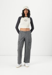 Grey cargo pants with side pockets, a fitted white and navy long-sleeve crop top featuring a sun graphic, and a light grey cap. White sneakers.