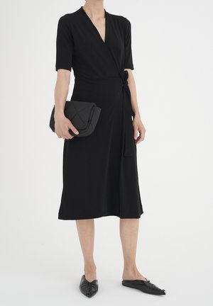 Czarna sukienka kopertowa z miękkiego materiału, z krótkimi rękawami, wiązana w talii. W zestawie pikowana czarna kopertówka i czarne płaskie buty.