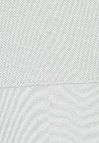 Biała tkanina z teksturowanym splotem o delikatnym połysku, gładkimi obszarami i szczegółowym przeszyciem wzdłuż szwu.