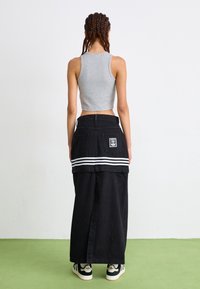 Grå kort topp och en svart jeanskjol med vita ränder vid midjan, tillsammans med svart och vita sneakers på en grön yta.