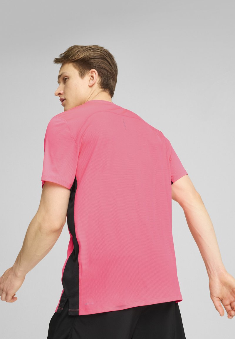 Camiseta deportiva en un vibrante color rosa, con mangas cortas, un tejido texturizado y paneles laterales negros. Diseñada para ofrecer comodidad y flexibilidad.