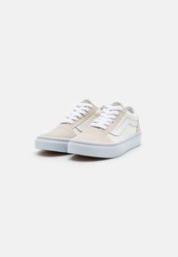 Zapatillas de ante beige con acentos blancos, que presentan cordones, suelas de goma y un diseño clásico de caña baja. Superficie texturizada y estilo minimalista.