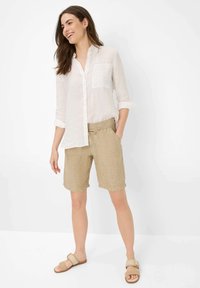 Witte linnen overhemd met knopen en een zak, gecombineerd met lichtbruine linnen shorts. Model draagt beige sandalen. Eenvoudige, gestructureerde stoffen.