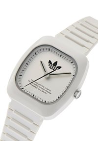 Neljane valge kell tekstureeritud silikoonrihmaga, minimalistlik hõbedane ja must nägu, millel on Adidas logo ja mustad tundemarkerid.