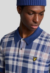 Polo a scacchi blu e bianchi, con colletto, tre bottoni e un piccolo logo giallo. Tessuto morbido, maniche corte.