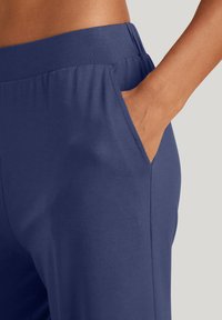 Marineblauwe rekbroek met een gladde textuur, elastische tailleband en zijzakken. De stof lijkt lichtgewicht en flexibel te zijn.