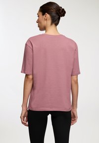 Jasnoróżowa, krótkiego rękawa koszulka z okrągłym dekoltem i luźnym krojem. Miękka faktura materiału, proste wykończenie i staranne szwy.