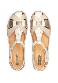 Sandales en cuir beige clair avec un design à lanières croisées, accents métalliques, perforations pour la respirabilité et détails en jute tressé.