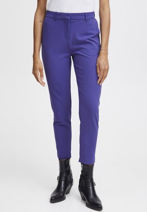 Pantalons violet fuselés avec une texture lisse, présentant une poche frontale et une taille avec passants de ceinture, associés à des bottines noires.