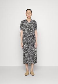 Vestido de estampa de leopardo em preto e branco, com mangas curtas em forma de puff, frente com botões e comprimento midi, combinado com sapatos bege de deslizar.