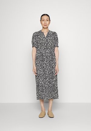 Vestido de estampa de leopardo em preto e branco, com mangas curtas em forma de puff, frente com botões e comprimento midi, combinado com sapatos bege de deslizar.