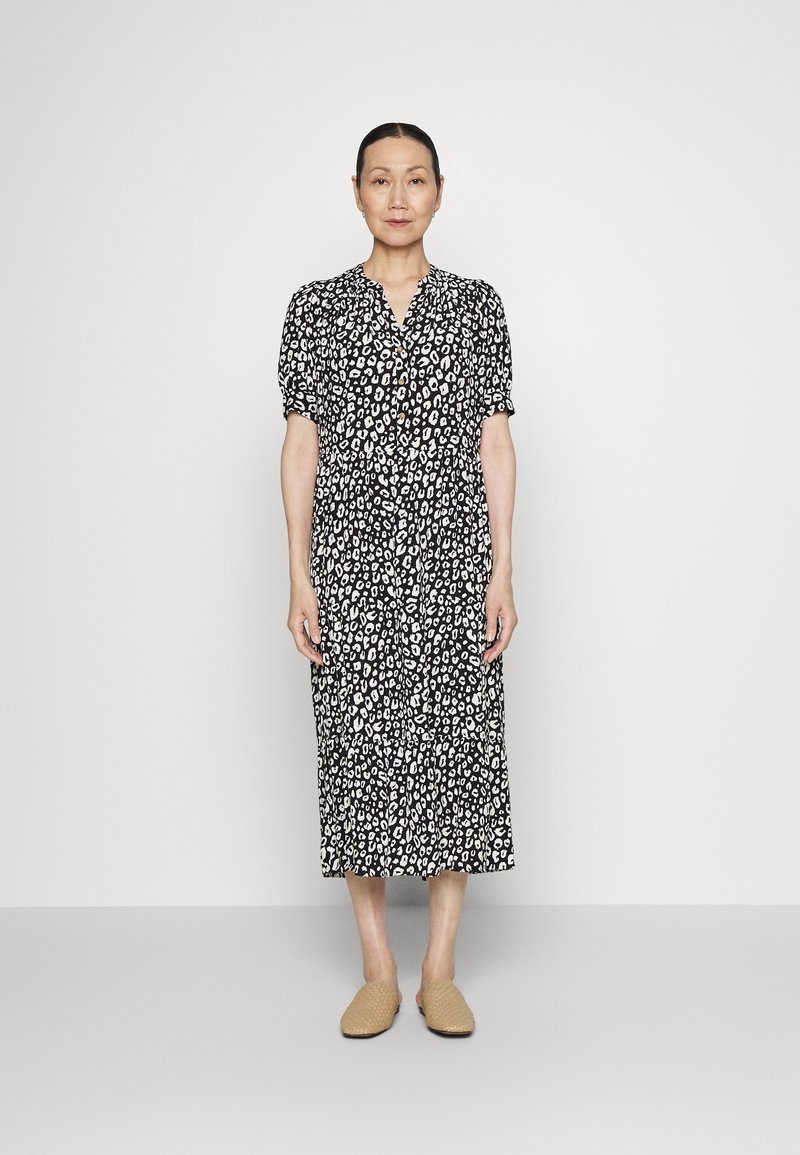 Vestido de estampa de leopardo em preto e branco, com mangas curtas em forma de puff, frente com botões e comprimento midi, combinado com sapatos bege de deslizar.