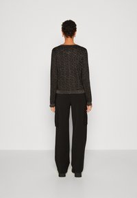 Czarny sweter dzianinowy z textured wzorem, długimi rękawami oraz ściągaczami na mankietach i dole, w połączeniu z luźnymi czarnymi spodniami.