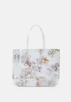 Biała torba tote marki Ted Baker z przezroczystym, kwiatowym nadrukiem, złotym logo i dwoma paskami na ramię na jednolitym tle.