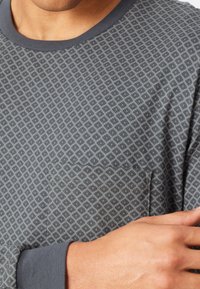 Chemise �à manches longues grise à motif géométrique. Elle présente un col rond et une poche sur la poitrine avec des coutures contrastées.
