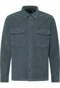 Camicia di velluto a coste color verde scuro con chiusura a bottoni, due tasche sul petto e colletto. Presenta una texture a costine verticali e un design leggermente sartoriale.