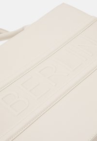 Sac en cuir crème avec un détail embossé "BERLIN" sur le devant. Texture lisse, design minimaliste et forme structurée.