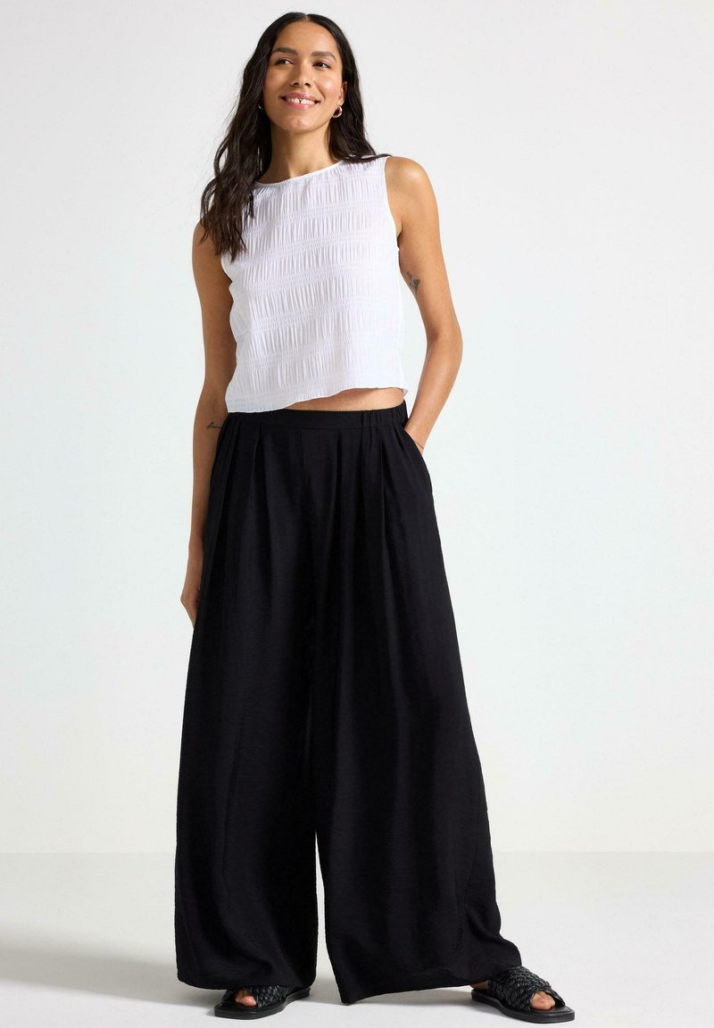 Hvid, cropped, ærmeløs top med teksturerede striber, parret med løse, højtaljede sorte wide-leg bukser. Sorte sandaler med vævet design.