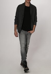 Mörkgrå stickad cardigan med stora knappar, nedtill med en svart t-shirt och ljusgrå jeans. Svarta stövlar kompletterar outfiten.