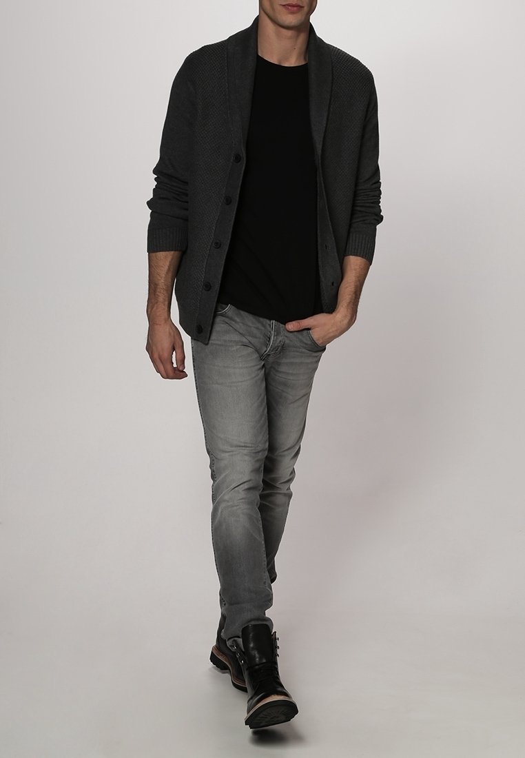 Mörkgrå stickad cardigan med stora knappar, nedtill med en svart t-shirt och ljusgrå jeans. Svarta stövlar kompletterar outfiten.