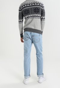 Pull gris à motifs avec un design de flocons de neige, associé à un jean bleu clair et des baskets blanches, mettant en valeur un pantalon retroussé et une coupe décontractée.
