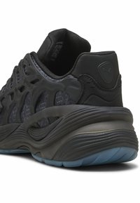 Černá sportovní bota s síťovaným svrškem a tvarovanými plastovými akcenty, vybavená silnou, zakřivenou gumovou podrážkou a texturovaným podpatkem.