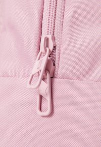 Tela de mochila rosa con una superficie texturizada, que cuenta con un zipper con tiradores a juego en rosa y un pequeño detalle de logotipo.