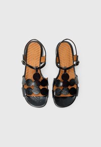 Melnas ādas sandales ar platu zoli, atvērtu dizainu un apļveida fakturētām rotājuma detaļām. Regulējams potītes siksniņa ar sprādzi.