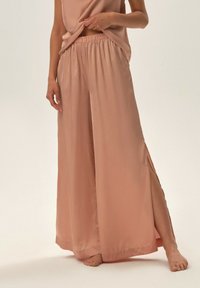 Jasnoróżowe satynowe spodnie o szerokich nogawkach z elastycznym pasem i bocznymi rozcięciami, zestawione z dopasowanym, bezrękawnikowym topem. Miękka faktura, minimalistyczny design.