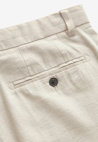 Pantaloni din in bej cu o textură netedă, având un buzunar pe partea din spate cu un nasture negru și detalii de cusătură subtile.