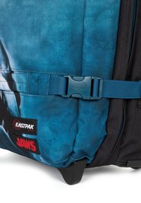 Modrý látkový batoh s černými akcenty, vybavený uzávěrem na přezku, s logy "EASTPAK" a "JAWS" a s texturovaným povrchem.
