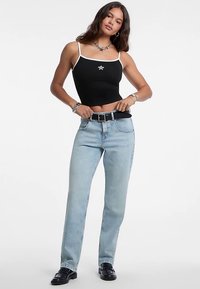 Černý krátký top s bílými ramínky a hvězdným emblémem, doplněný světle modrými džíny s rovnými nohavicemi a černými botami.