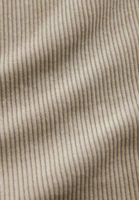 Tan corduroy fabric with prominent vertical ribbing. Soft texture with subtle sheen. The pattern is consistent and evenly spaced.