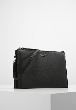 Černá kožená peněženka na zápěstí s texturou, zlatým zipem a logem "kate spade new york" na přední straně, umístěná na bílém povrchu.