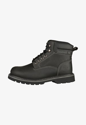 Botte de travail en cuir noir avec un col rembourré, des œillets en métal et des coutures contrastantes. Dotée d'une semelle en caoutchouc texturé pour une meilleure adhérence.