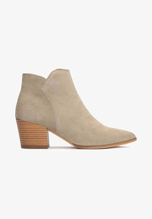 Botte de cheville en daim beige avec un bout pointu et un talon empilé moyen. Présente un design découpé et une texture lisse.
